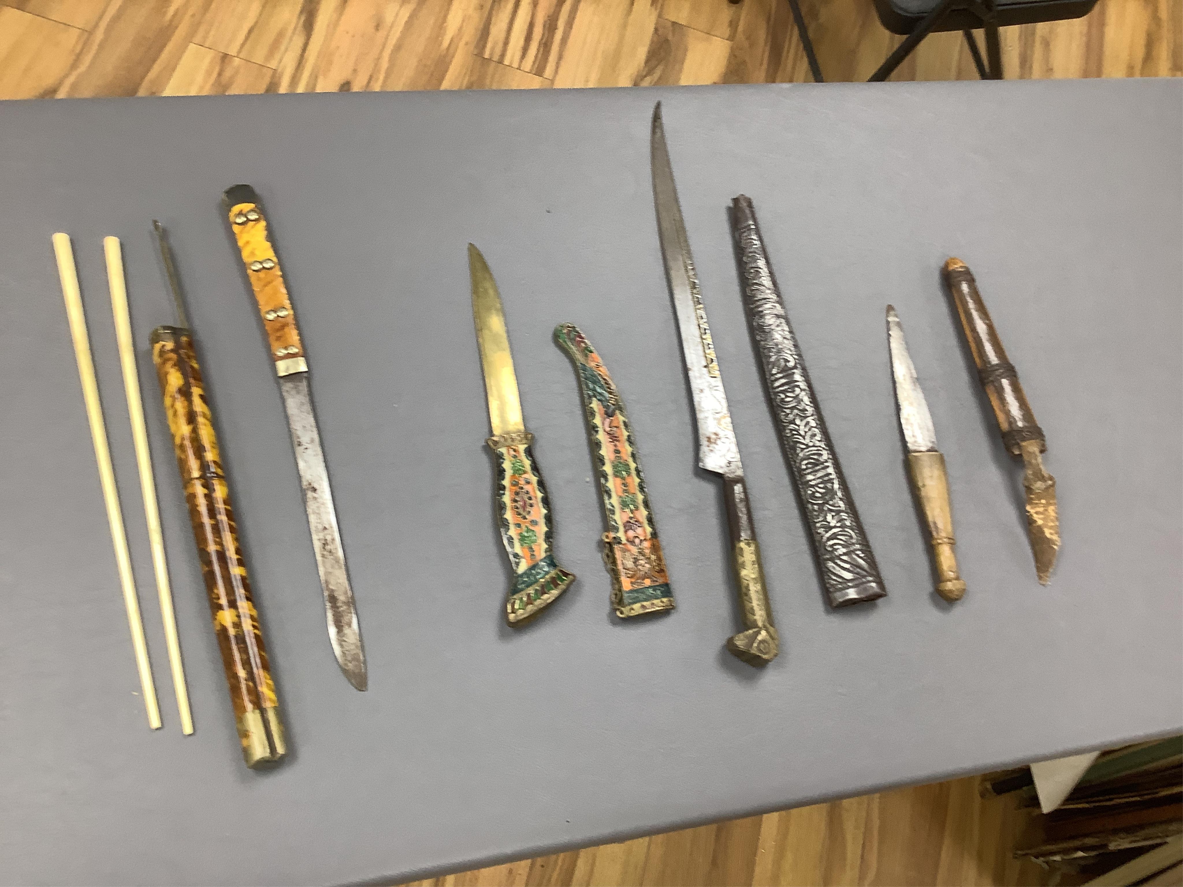 Eighteen assorted world weapons comprising a silver jambya (pommel missing), a knobkerry, a dha, two kris (one with handle missing), a lohar, three kukris, a djambok, a Chinese trousse, a chora, a flyssa, five others and